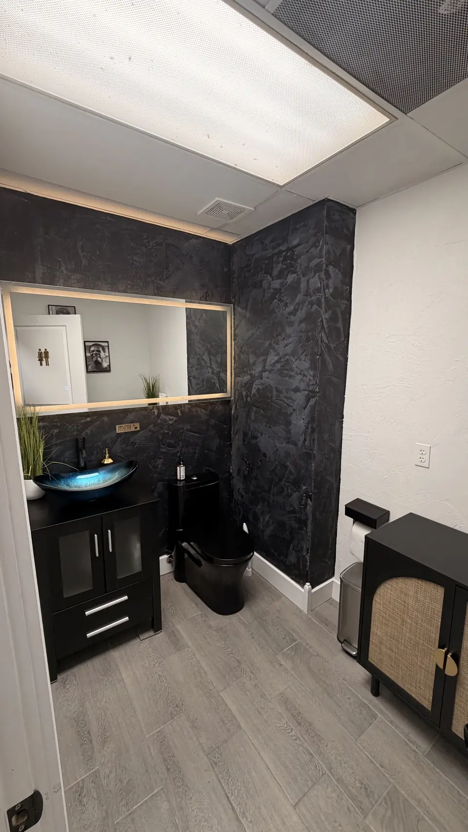 Restroom with dark plaster walls, black vanity and glass vessel sink