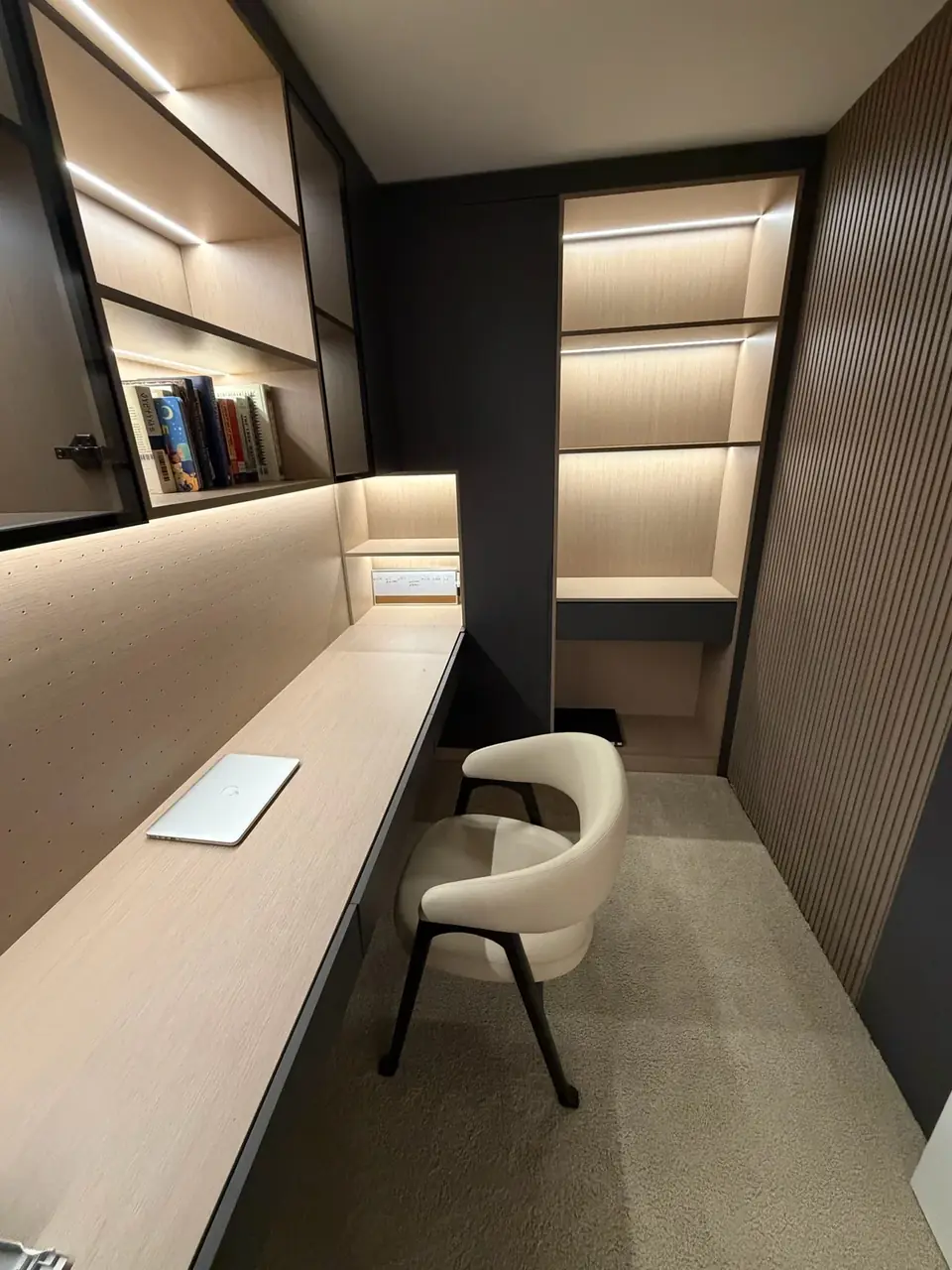 Home office with built-in desk, lit oak shelving and fluted wall panels