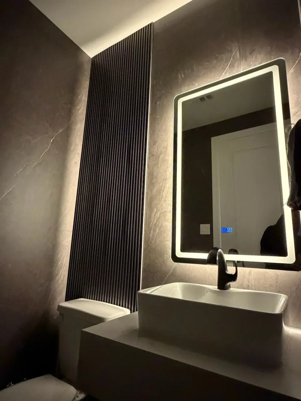 Powder room with backlit mirror, vessel sink and stone-look walls